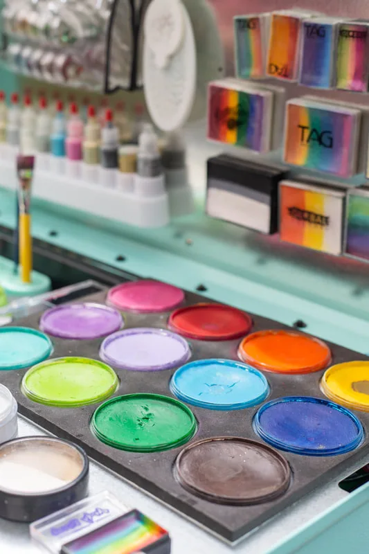 A teal festival face painters kit with rainbow glitter, rainbow split cakes, and solid face painting cakes