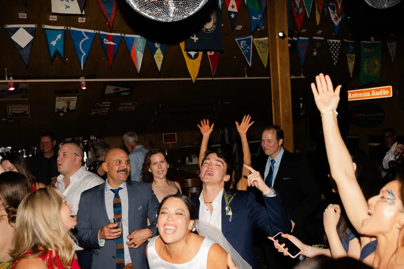 A group of smiling adults singing and dancing at a wedding in Sausalito, California. The group is sporting fun glitter and face paint from the Glitter Bar.