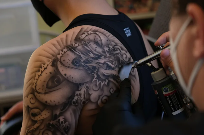 A young light skinned person modeling a realistic dragon airbrush tattoo on their shoulder in San Mateo, California