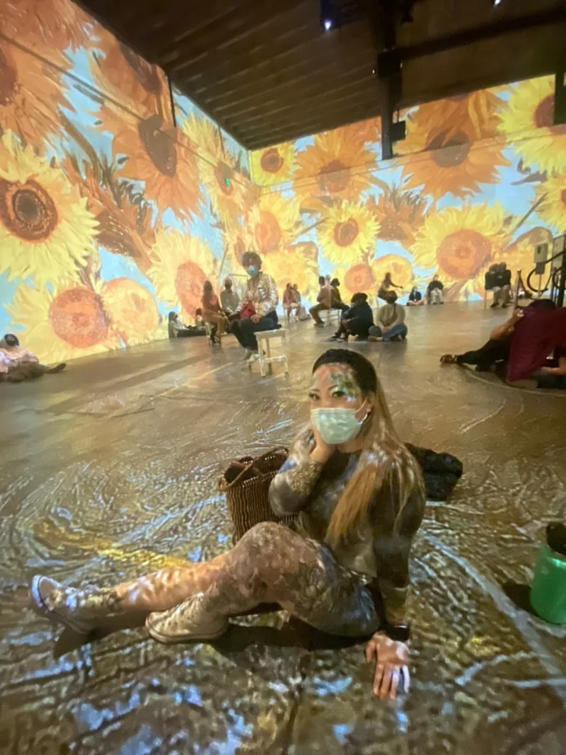 A woman with sunflower face painting sits in the middle of the immersive Van Gough exhibit, San Francisco