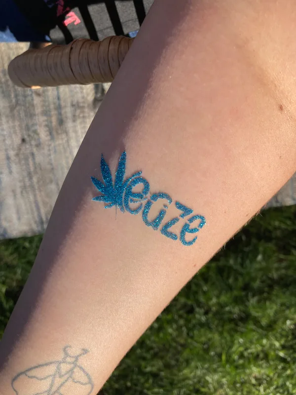 A glitter tattoo from a corporate event features a cannabis leaf and the company logo "Eaze" in sparkly blue glitter