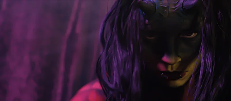 A close up of a person face and body painted as a dragon, looks intensely into the camera